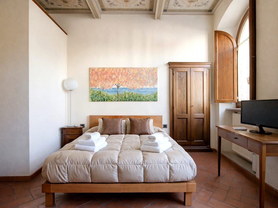 camera-michelangelo-residence-epoca-arezzo Camera matrimoniale Michelangelo con soffitto decorato, armadio in legno e TV