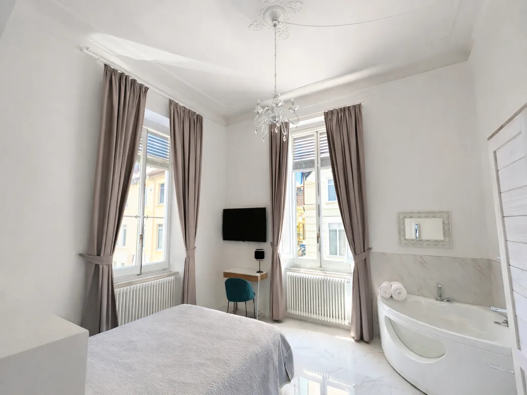 camera-suite-con-vasca-angolare-viareggio.webp Vista completa della suite con letto matrimoniale e vasca idromassaggio a Viareggio