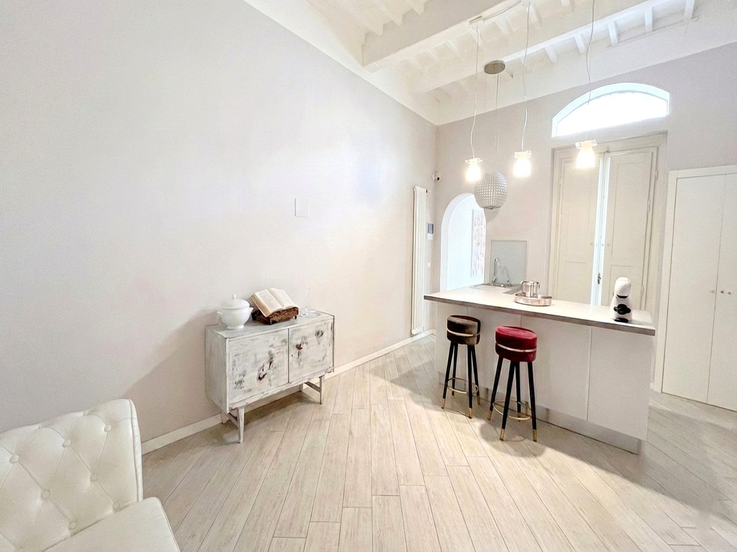short-lets-arezzo-zona-living-camera-114 Zona living collegata alla camera 114 con bancone, sgabelli e soffitto a travi bianche