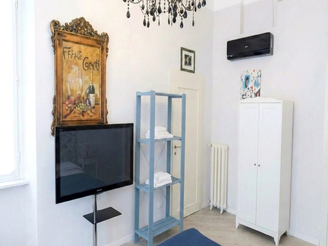 soggiorni-brevi-in-toscana-camera-114-con-tv Camera matrimoniale 114 con televisore, armadio bianco e scaffale porta asciugamani