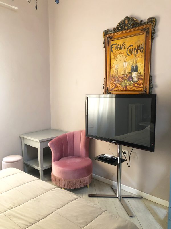 b-and-b-arezzo-camera-114-con-tv Angolo della camera 114 con televisore, poltrona rosa e quadro decorativo